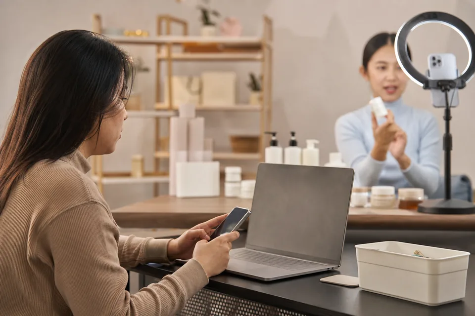 Moderator with a phone and a laptop turned away next to a live shopping set with a ring light