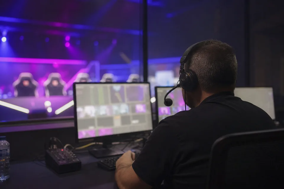 Moderator at a desk with two monitors turned away from the camera during a live esports broadcast